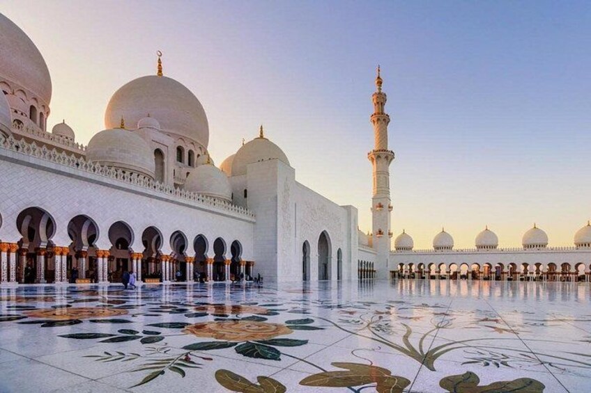 A mosque with large domes, a tall minaret, and a tiled courtyard with floral patterns. 1