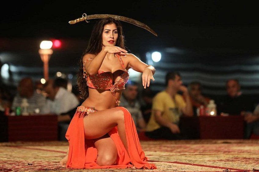 A person in a red outfit performing an act with a sword in a dimly lit outdoor setting. 2