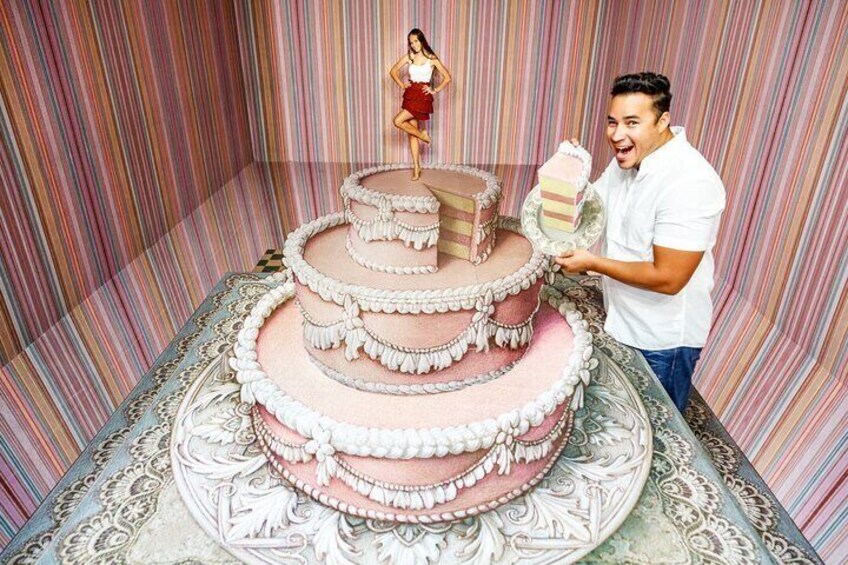 A multi-tiered cake with intricate white and pink icing decorations, a woman in a red dress standing on top, and a man holding a slice of cake. 5