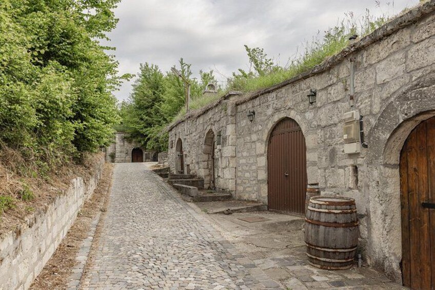 A cobblestone street with stone buildings, wooden doors, and barrels. 2