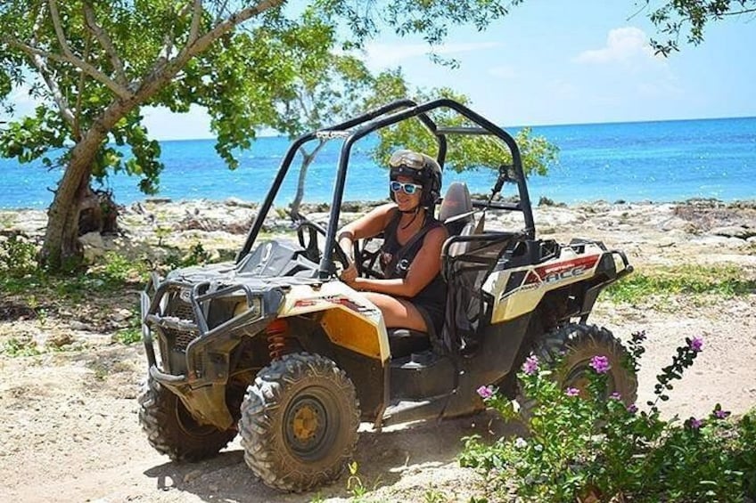 Iemand rijdt op een quad over een stoffig pad in de buurt van een strand, met de oceaan op de achtergrond. 2