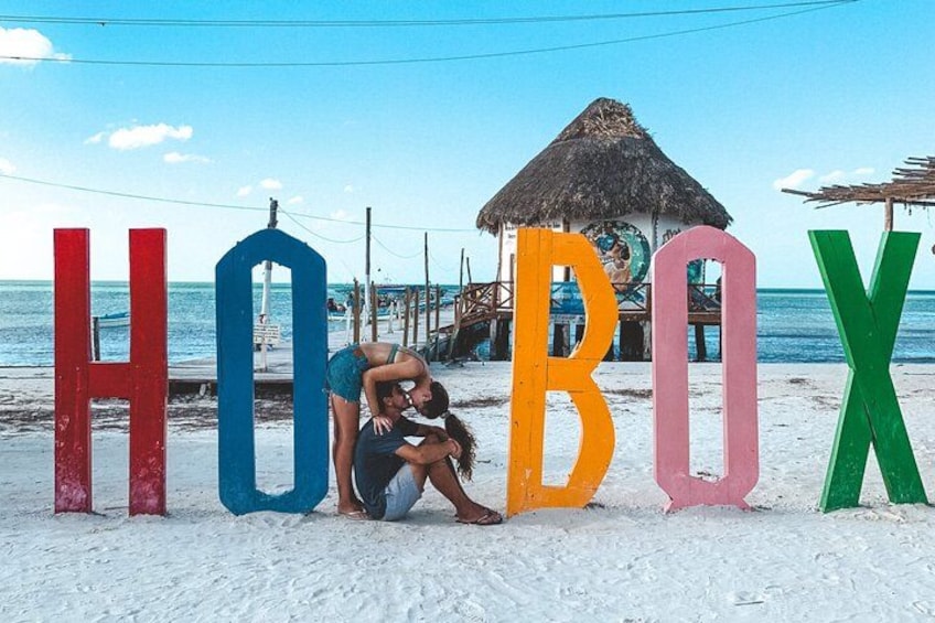Una playa con letras de colores que deletrean 'HOBOX' y una cabaña de techo de paja al fondo. 3