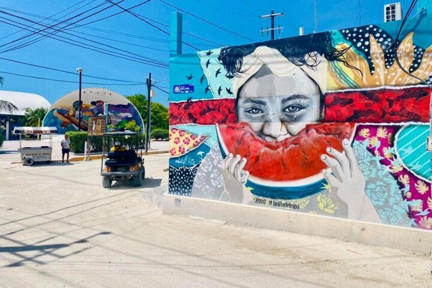 Un mural que muestra a una persona sosteniendo una sandía, un autobús y un camión en una calle. 4