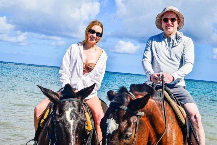 To personer rider på heste på en strand med havet i baggrunden. 2