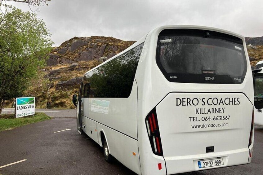 A white tour bus with 'DERO'S COACHES KILLARNEY' and contact information on the back. 3