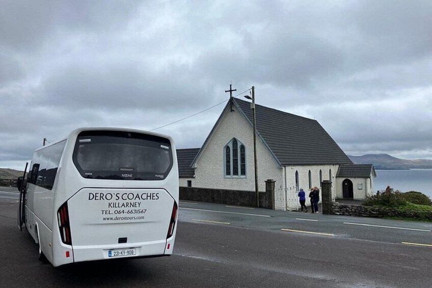 A white van with 'DERO'S COACHES' and contact information parked in front of a white church with a grey roof. 4