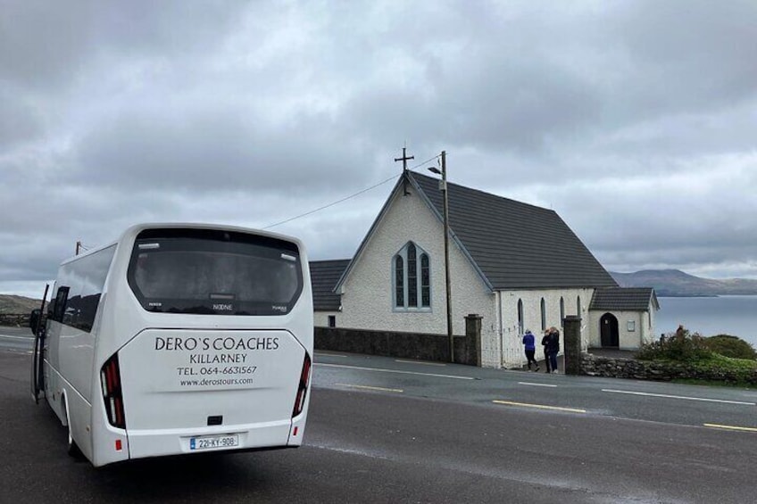A white van with 'Dero's Coaches' and 'Killarney' on the back, parked on a road with a white church in the background. 4