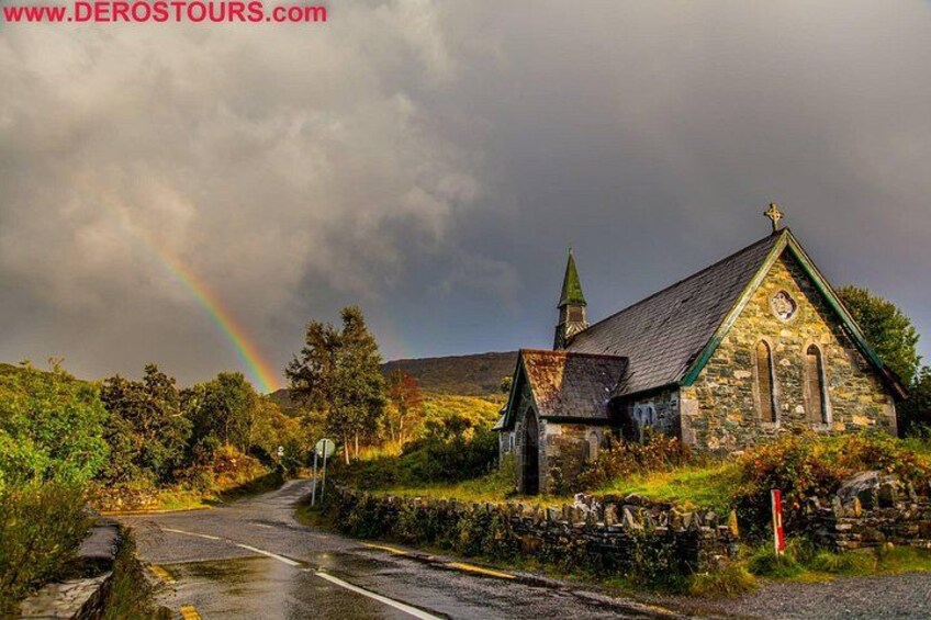 Une église en pierre avec un clocher, un arc-en-ciel et une route qui y mène. 4