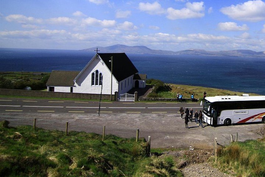 A coastal road with a white church, a parked bus, and a clear view of the sea and distant mountains. 3