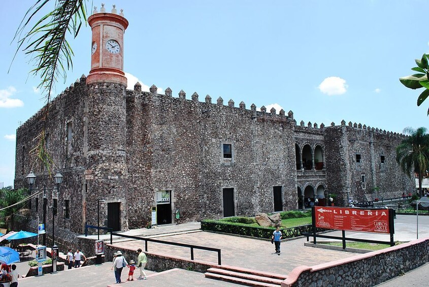 A historic stone building with a clock tower, a signboard, and a paved area with steps leading up to it. 3