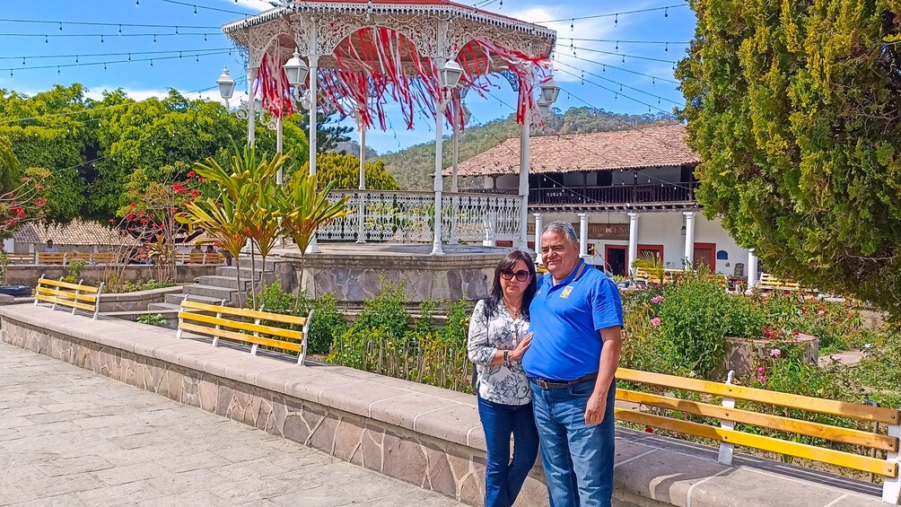 Un pabellón con decoraciones rojas y blancas, un banco de piedra y un edificio con techo de tejas al fondo. 1