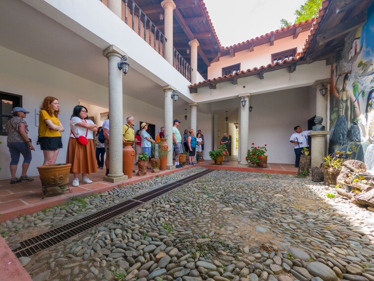 Un patio con gente alrededor, columnas, un mural y plantas en macetas. 2