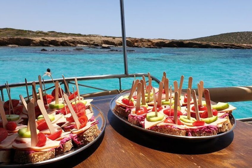 Two trays of fruit skewers on a boat with a view of a blue sea and rocky coastline. 1