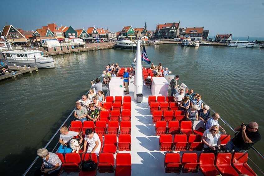 A boat with red chairs and passengers, docked at a harbor with buildings in the background. 3