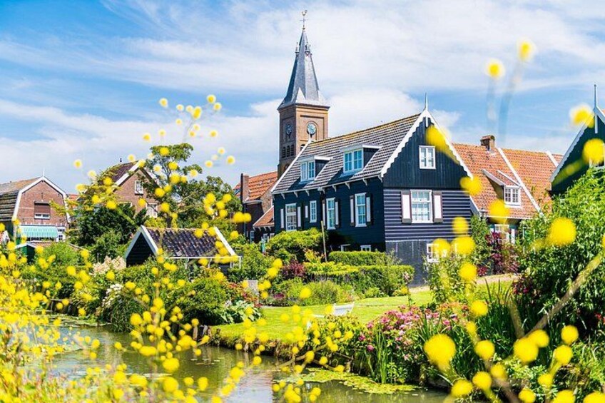 A Dutch village with traditional houses, a church, and a pond with yellow flowers. 5