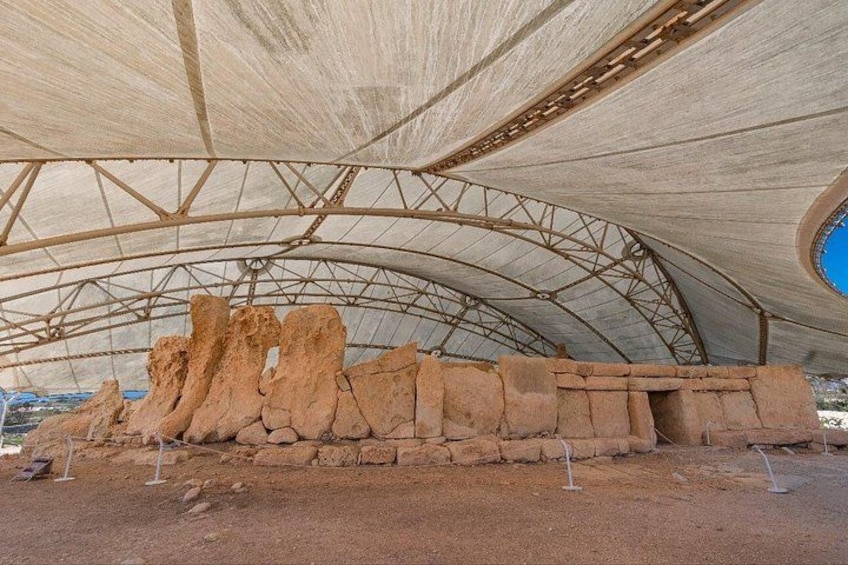 An archaeological site with large rock formations under a covered structure. 1