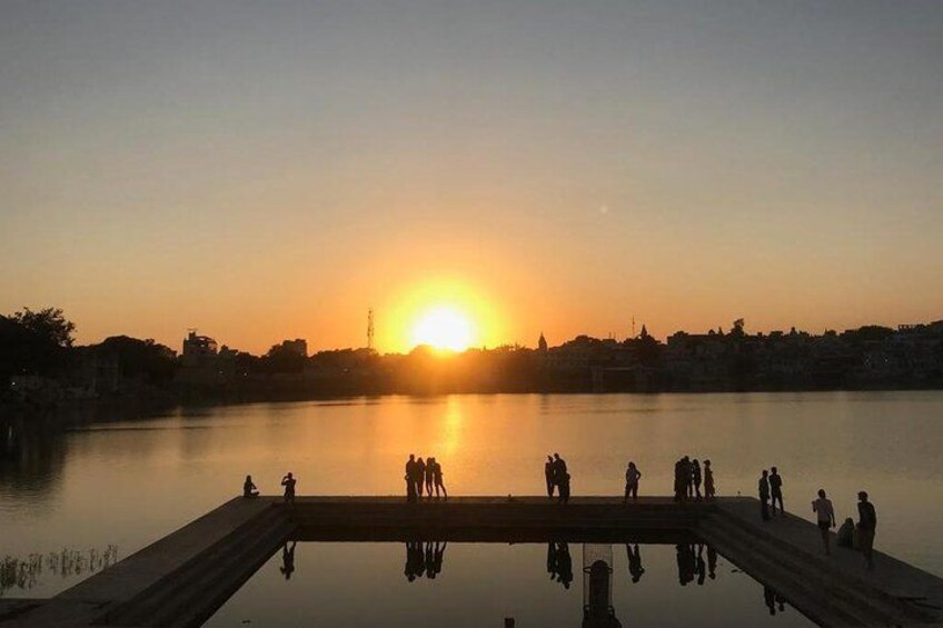 Een zonsondergang boven stilstaand water, met mensen op een steiger. 3