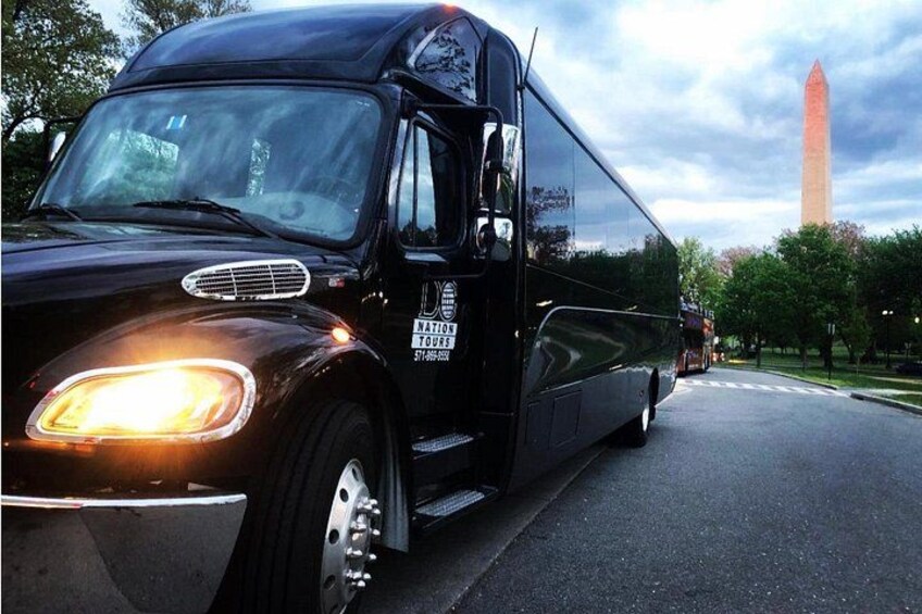 Un autocar noir, sur lequel on peut lire « NATIONAL TOUR » sur le côté, est garé sur une route, avec le Washington Monument en arrière-plan. 2