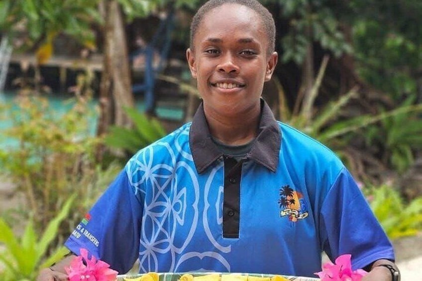 A person wearing a blue shirt with a logo, standing outdoors with greenery in the background. 4