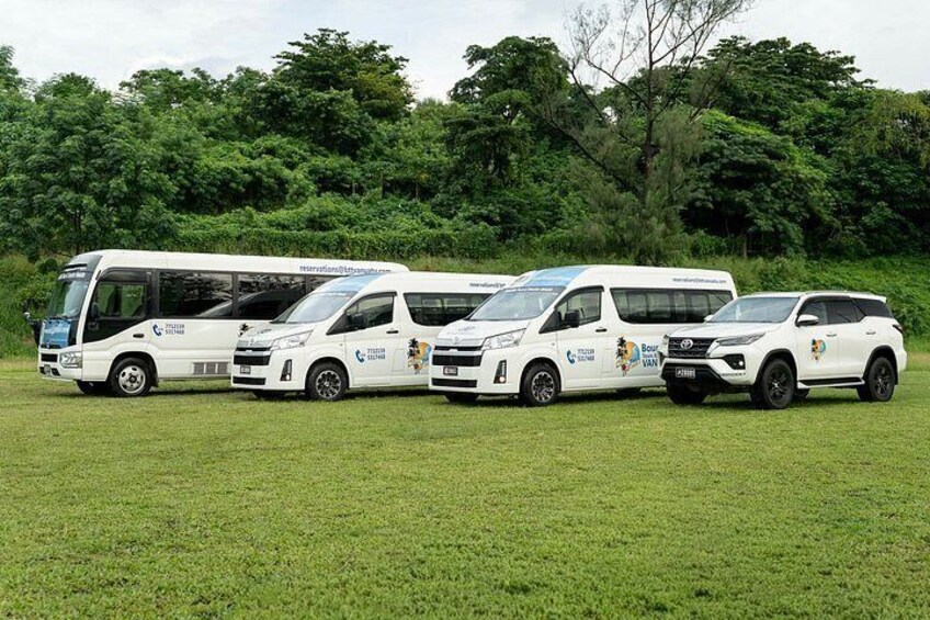 A row of white vehicles with logos, parked on a grassy field with trees in the background. 5