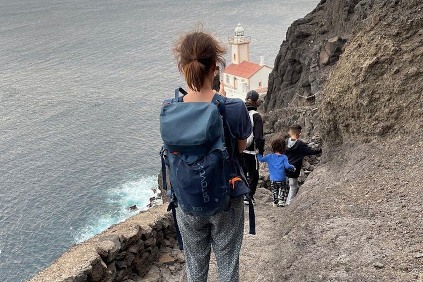 Une personne portant un sac à dos, debout sur une falaise surplombant l’océan, avec un phare en arrière-plan. 5
