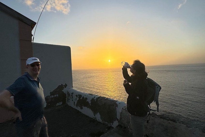 Deux personnes se tiennent près d’un mur, face à la mer, au moment du coucher du soleil. 2