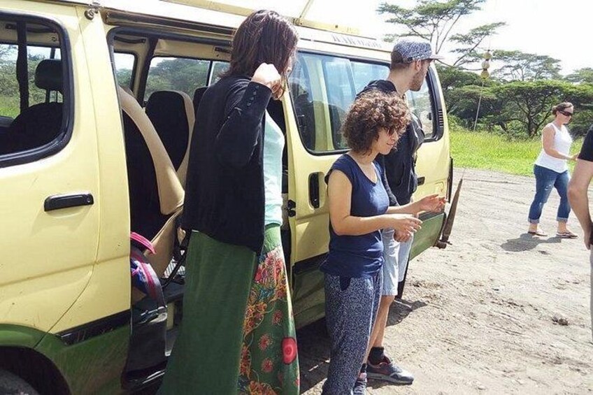 People boarding a yellow vehicle, a dirt road, and a grassy area. 4