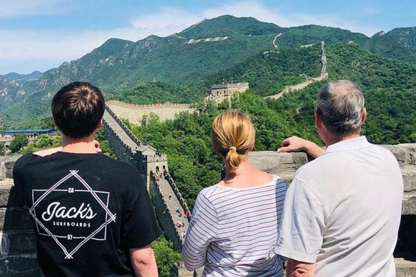 Tres personas observando la Gran Muralla China desde un punto elevado con vistas al paisaje. 2