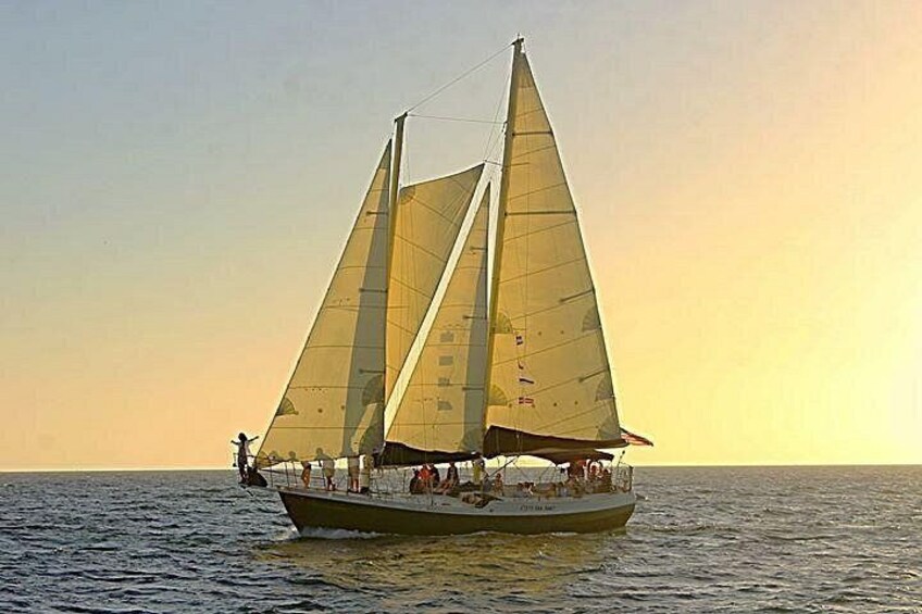Een zeilboot met meerdere zeilen op een rustige zee tijdens zonsondergang. 3