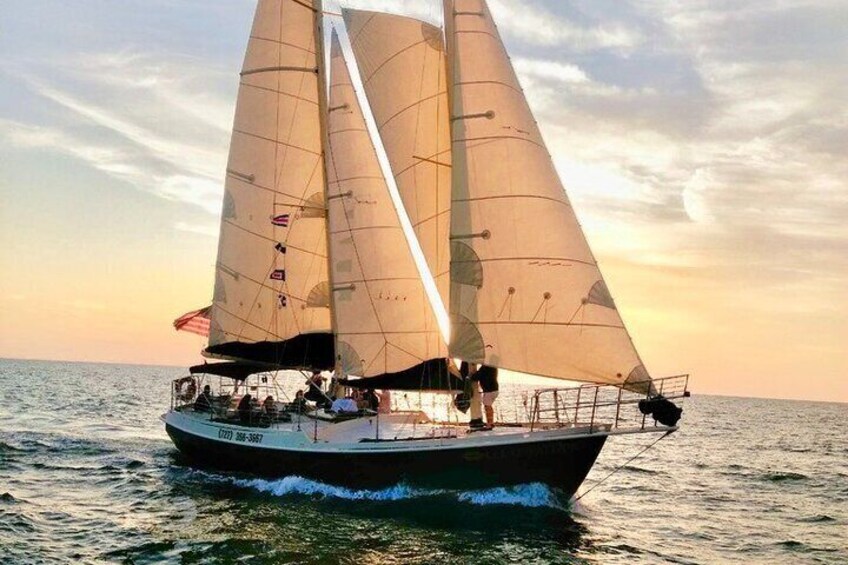 Un voilier avec plusieurs voiles sur l’eau, au coucher du soleil. 1