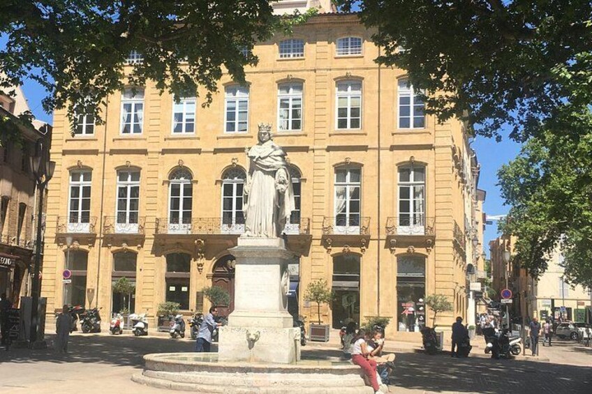 A statue in front of a yellow building with arched windows and a fountain. 5