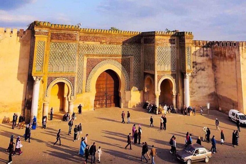 A historic gate with intricate designs, a large archway, and a crowd of people. 5