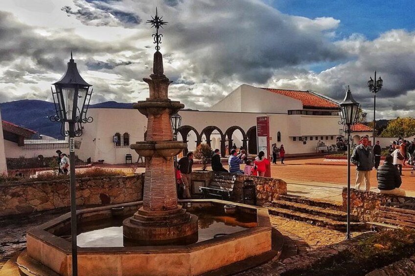 A fountain, a white building with arches, and people walking around. 4