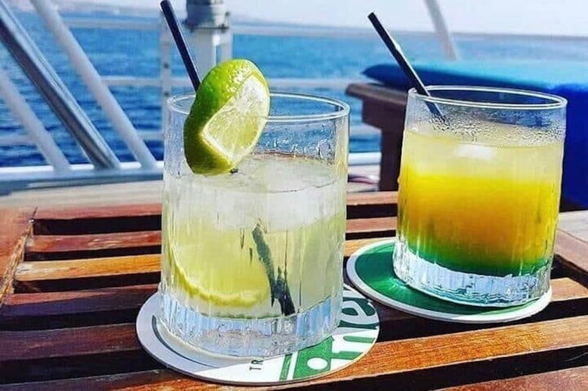Dos vasos de bebidas sobre una mesa de madera con vista al océano. 3