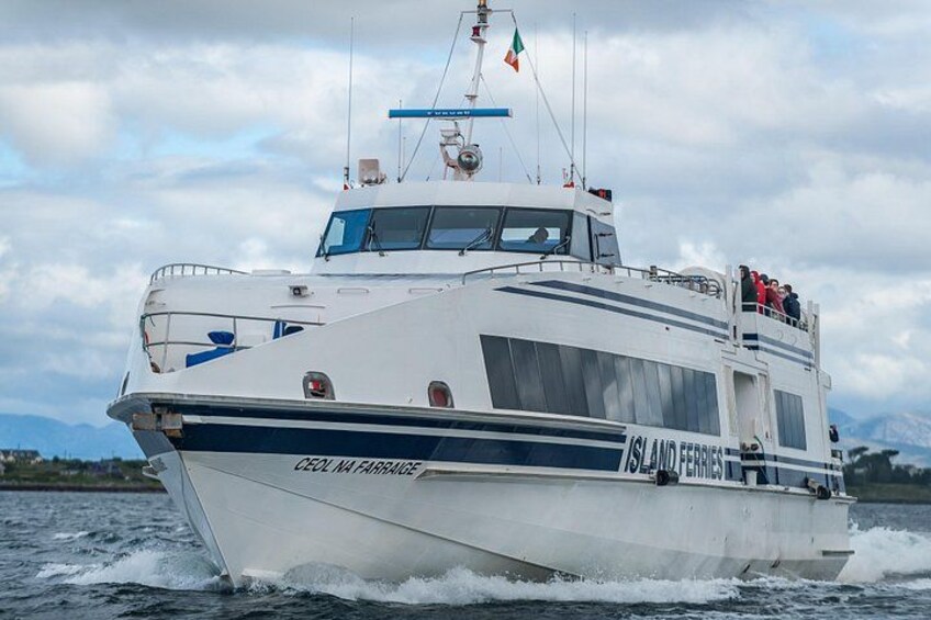 A white boat with 'Island Ferries' written on the side, moving on water with mountains in the background. 1