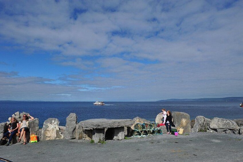 A rocky shoreline with people sitting on the rocks, a boat in the water, and a clear sky. 4