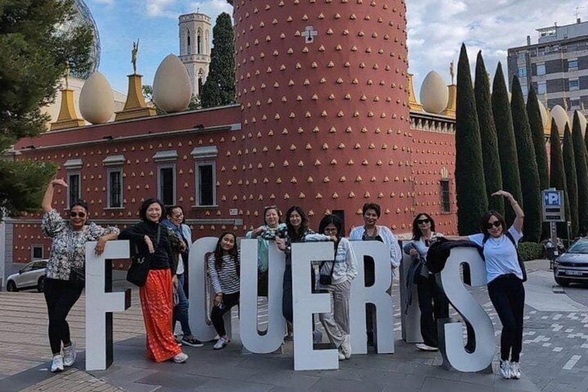 A group of people standing in front of a building with large letters spelling 'FICUERS'. 1