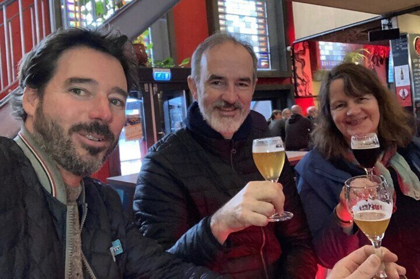 Three people holding glasses of beer in a bar with red decor. 4