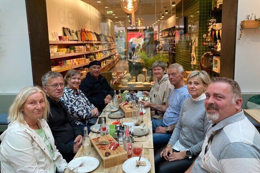 A group of people sitting at a table in a café with various food items and drinks. 5