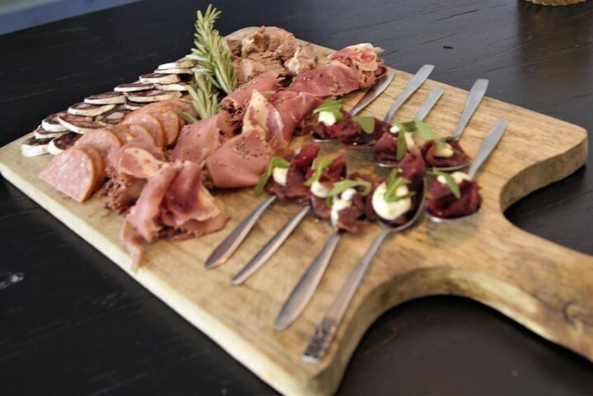 A wooden board with various meats, including sliced ham and prosciutto, garnished with rosemary and small greens. 4