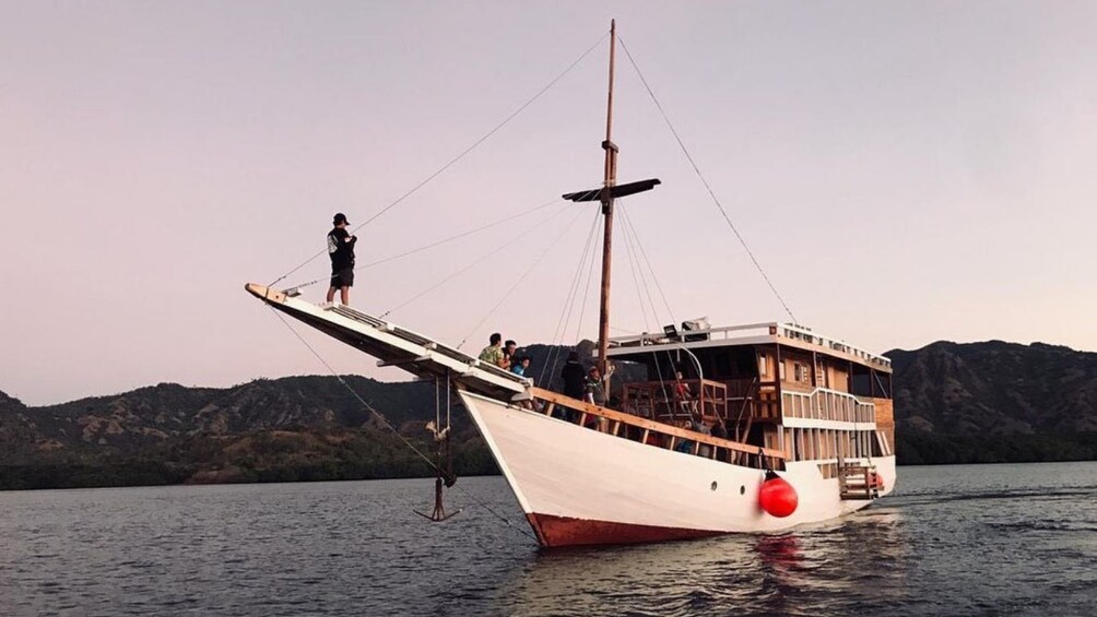 A white boat with a red buoy on calm water, a person standing on the bow, and a mountainous landscape in the background. 2