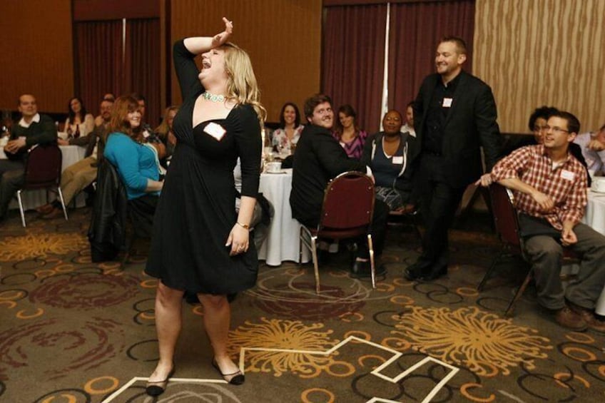 A woman in a black dress dancing in a room with a patterned carpet, surrounded by seated attendees. 2