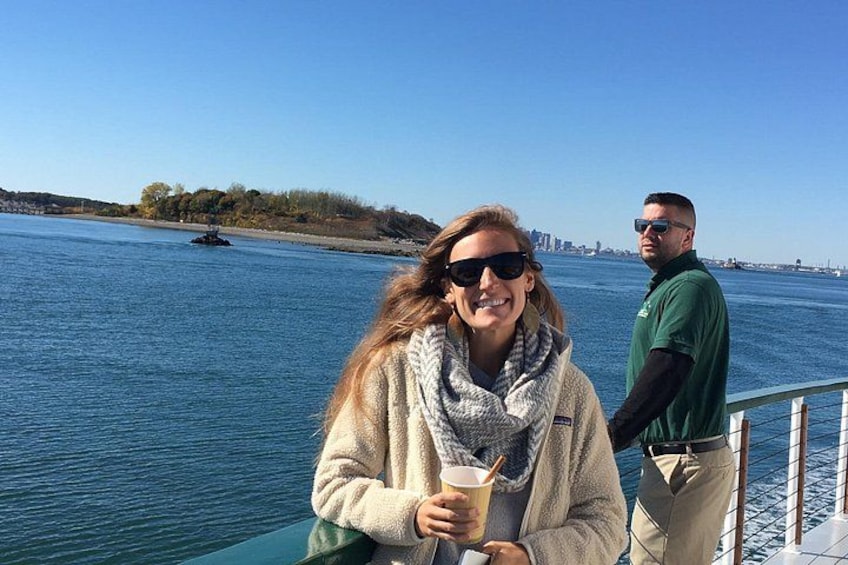 A person holding a drink, a railing, and a body of water with a distant shoreline. 2