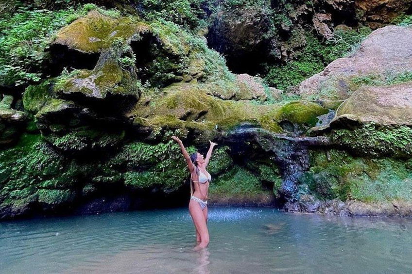 A person in a bikini standing in water with rocks and greenery in the background. 5