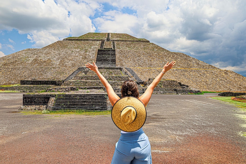 Una persona con le braccia alzate di fronte a una grande piramide. 1