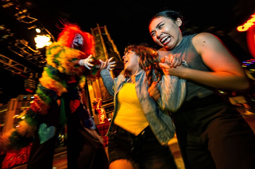 A person in a colorful costume with a mask and a feathered headdress, another person in a yellow top and denim jacket, and a third person in a sleeveless top and black pants. 3