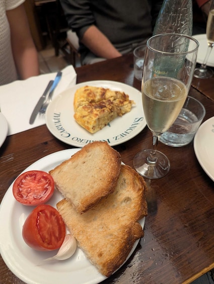 Lautasella on paahtoleipää, tomaattia ja valkosipulia, toisella lautasella lasillinen valkoviiniä ja viipale quiche-piirakkaa. 2