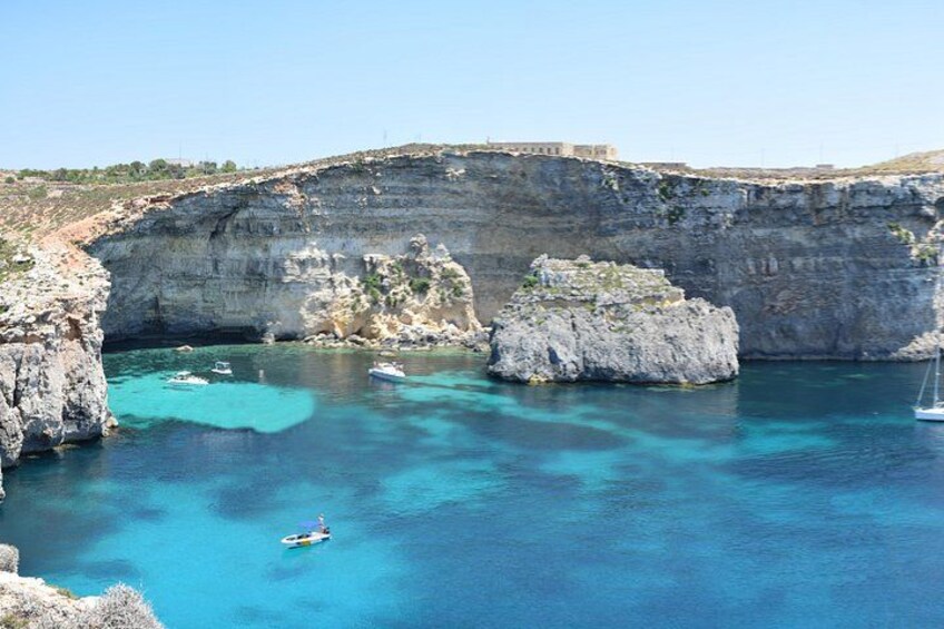 A coastal landscape with a rocky cliff, clear turquoise waters, and a small boat. 4