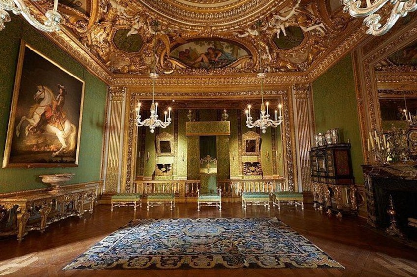 Una habitación opulenta con detalles dorados ornamentales, un candelabro grande y una alfombra detallada. 2