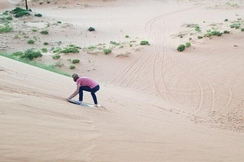Una persona con camisa rosa y pantalones azules baja por una pendiente arenosa con vegetación escasa. 2
